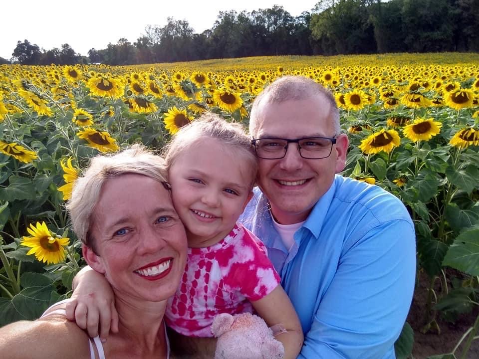 Image of Nate, his wife and youngest daughter in a sunflower field